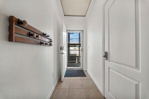 Un pasillo con un perchero de madera, una puerta con cerradura electrónica y vistas a un balcón con barandilla.