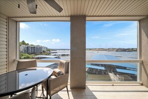 A balcony with a table and chairs, overlooking a waterfront with buildings and a bridge. - Land's End Condo - Ideal location & great view! (Osage Beach)