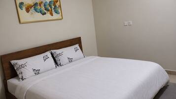 A neatly made bed with white bedding and patterned pillows, a wooden headboard, and a wall-mounted painting.