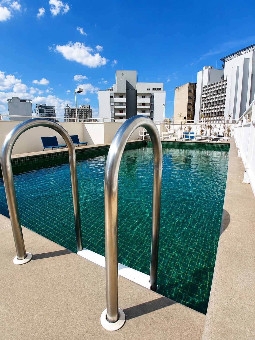 A rooftop pool with clear blue water, metal pool ladders, and a cityscape in the background.