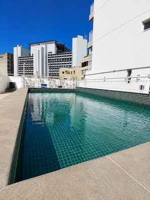 Une piscine dont le bord est recouvert de carreaux, entourée d’immeubles.