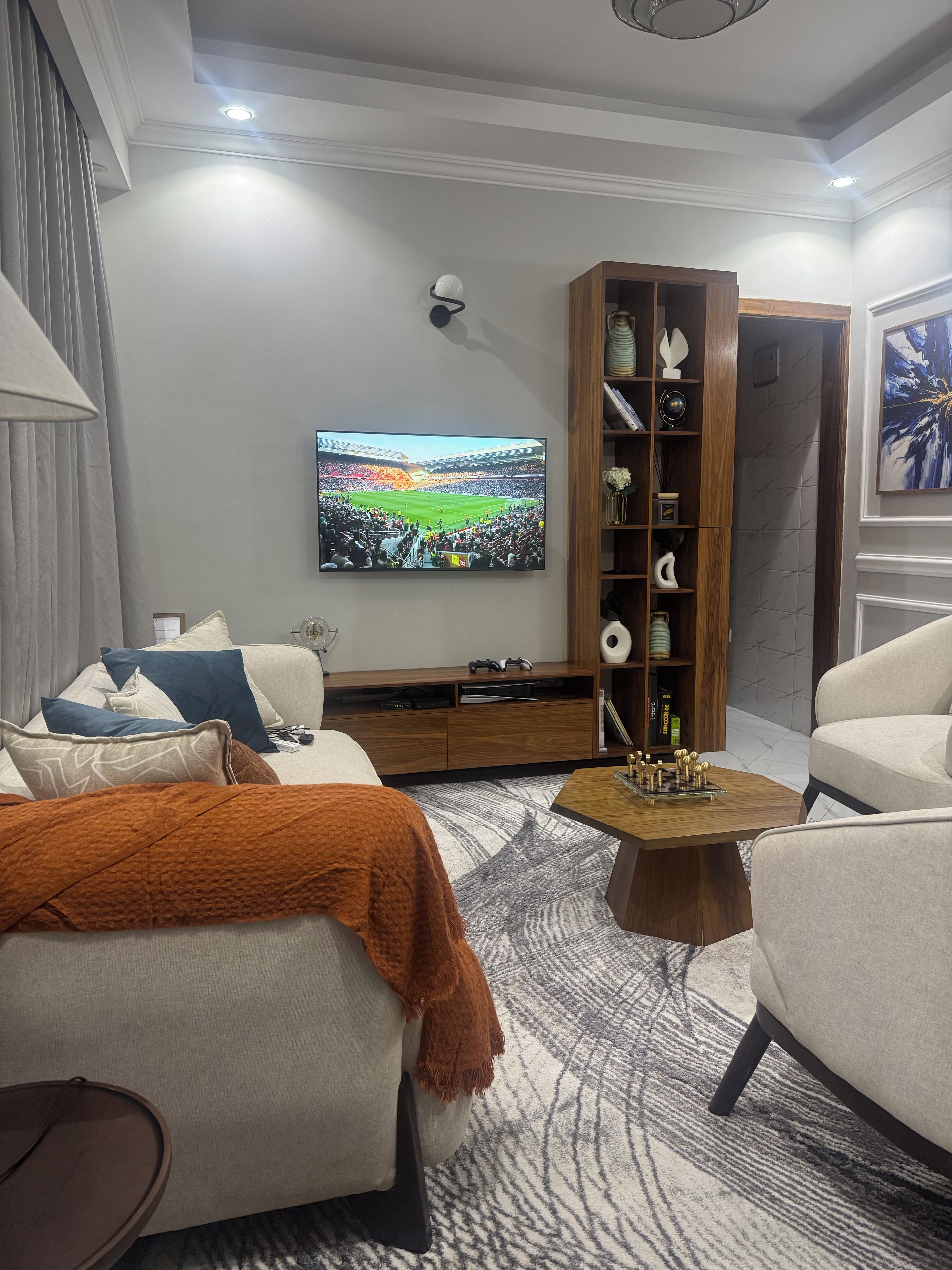 A modern living room with a flat-screen TV, a wooden entertainment unit, and a patterned rug.