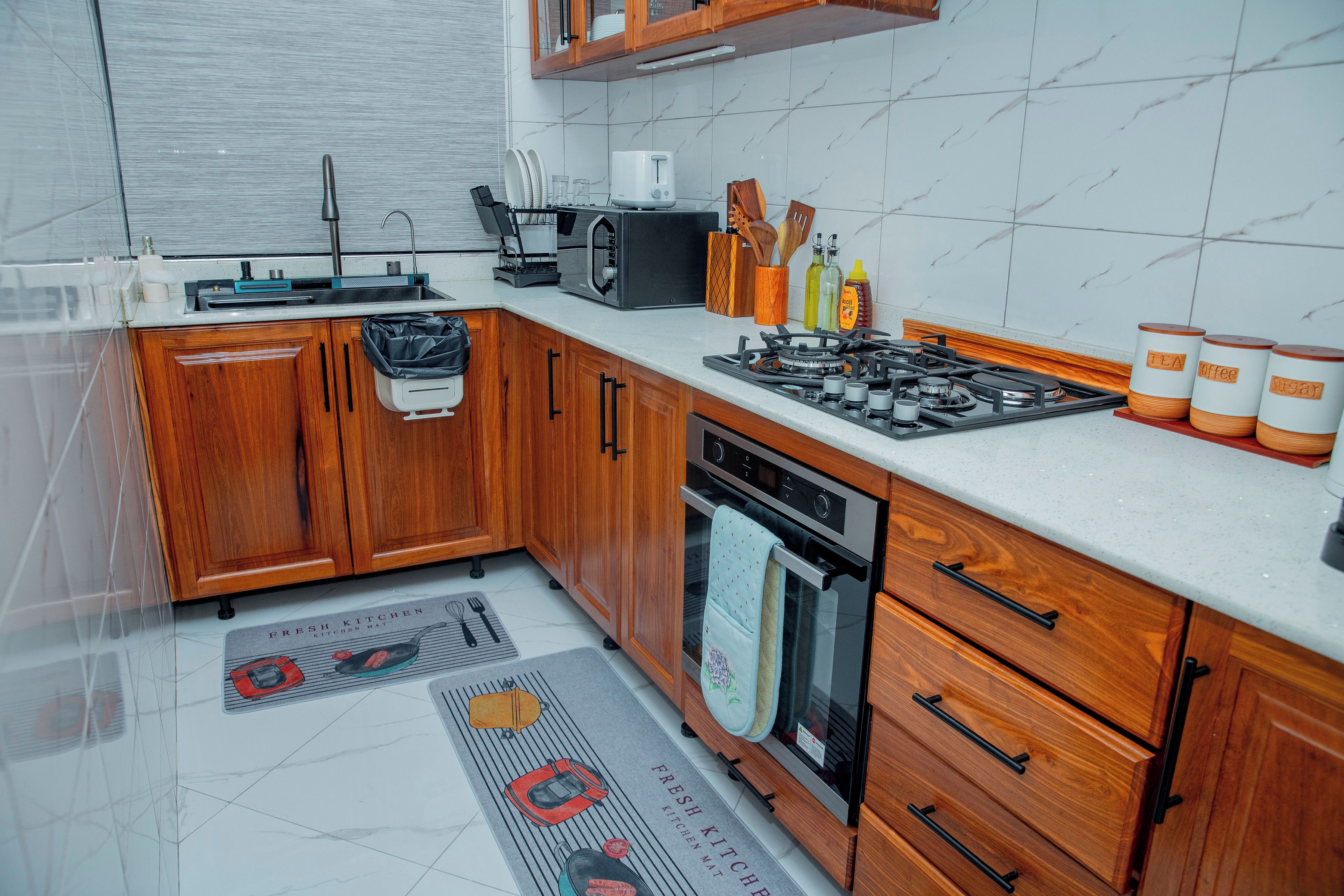 Une cuisine dotée de meubles de rangement en bois, d’une cuisinière à gaz, d’un four à micro-ondes et de divers ustensiles de cuisine.