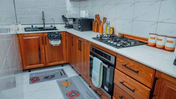 Une cuisine dotée de meubles de rangement en bois, d’une cuisinière à gaz, d’un four à micro-ondes et de divers ustensiles de cuisine.