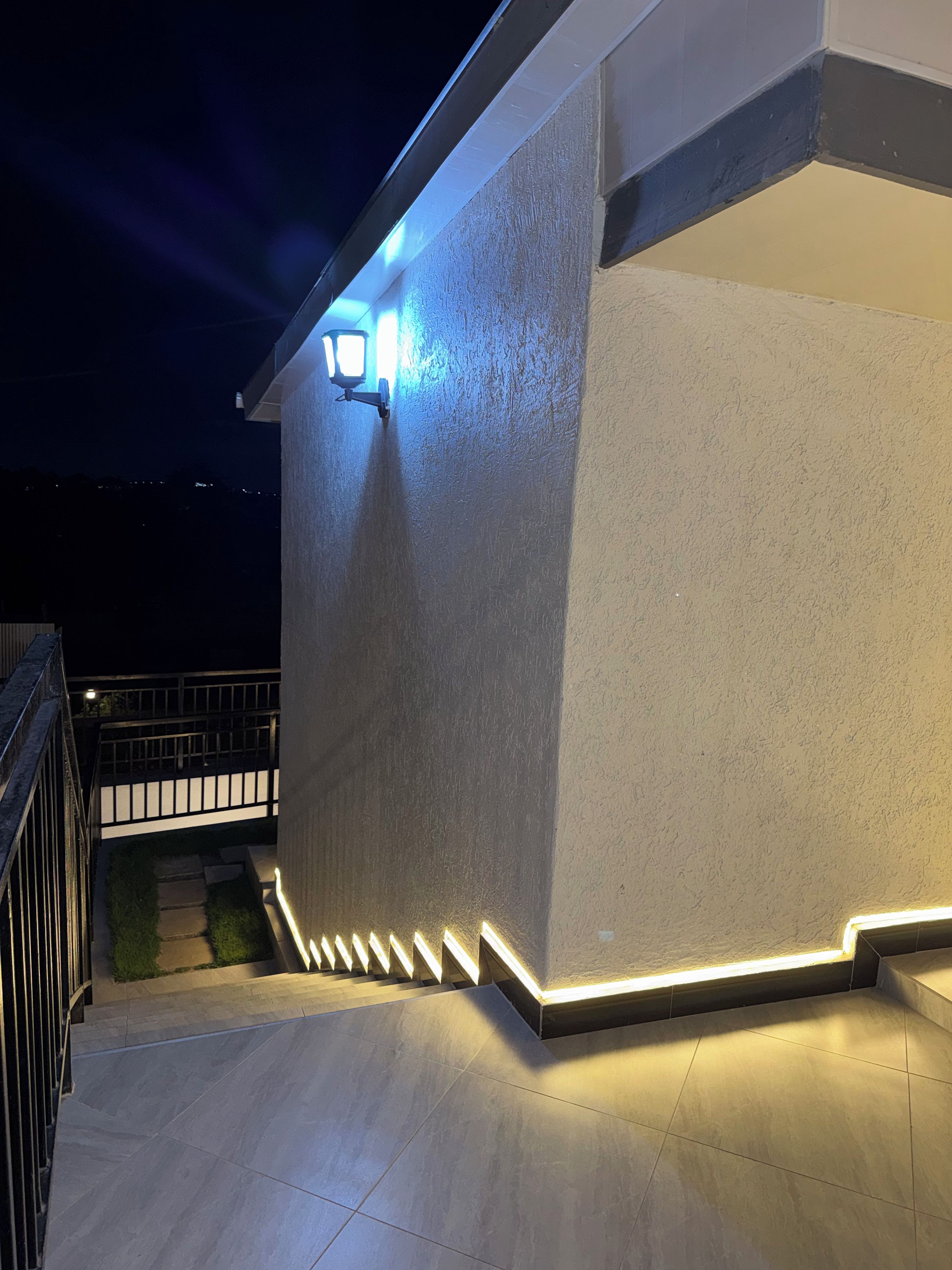 A building exterior at night with exterior lighting and a visible staircase.