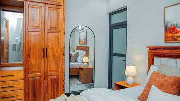 A hotel room with a wooden wardrobe, a bed with white bedding, a nightstand with a lamp, and a painting on the wall.