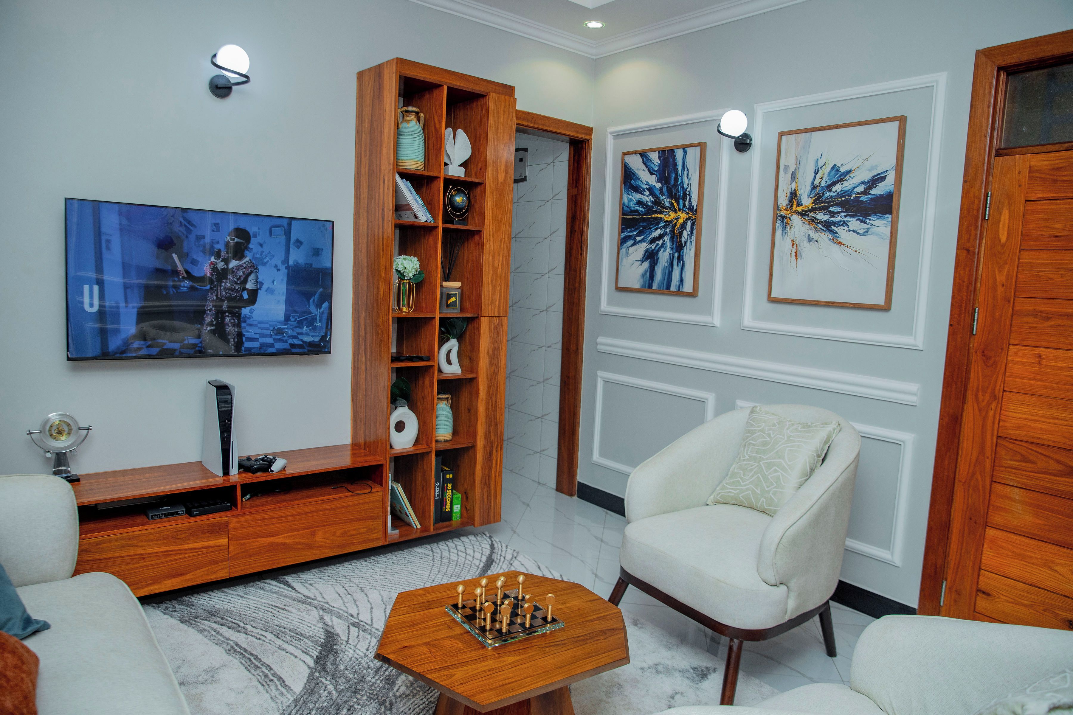 Un salon moderne avec un meuble de rangement en bois, un téléviseur à écran plat, une console de jeux et une table d’échecs.
