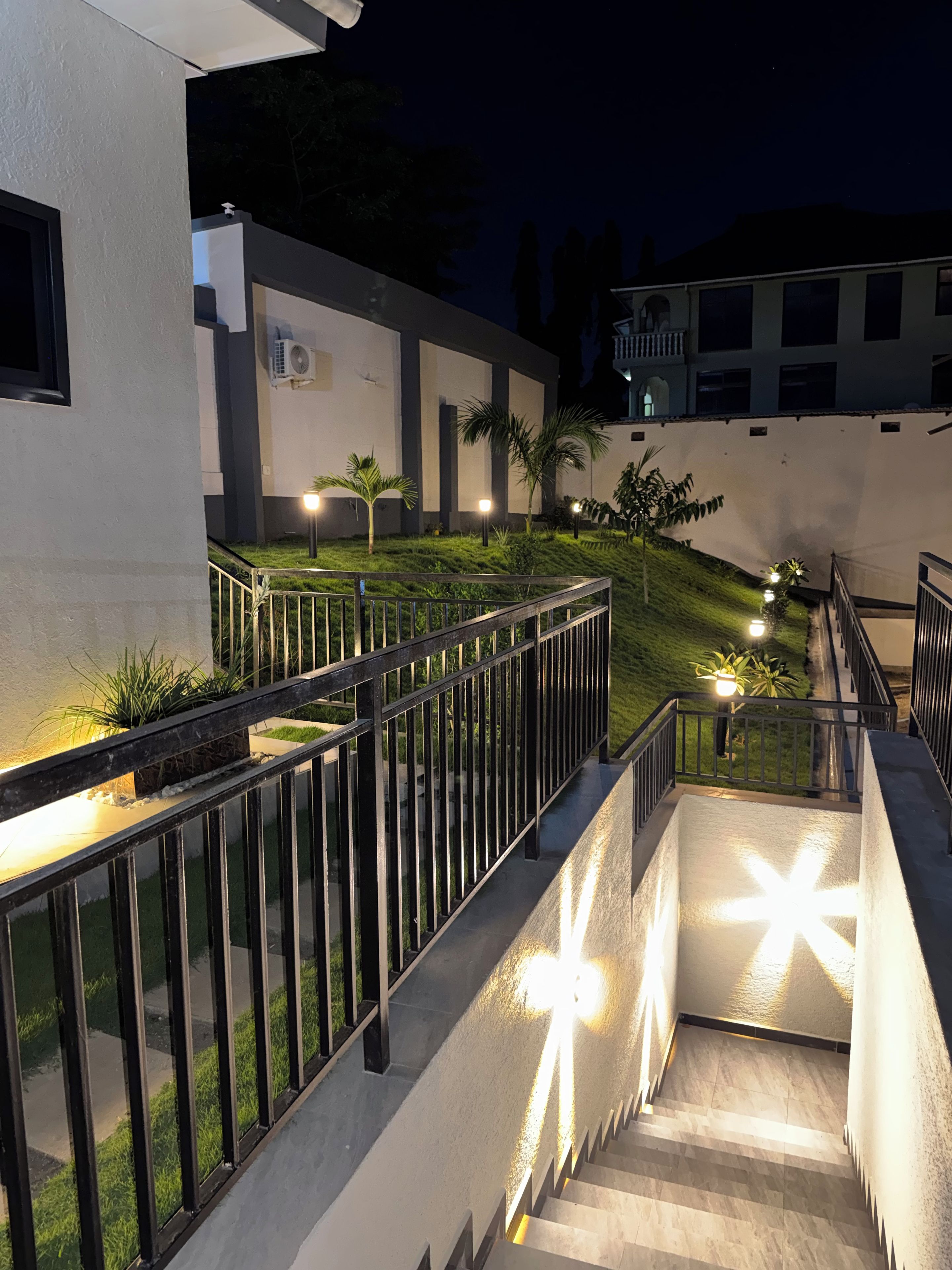 A nighttime view of a building's exterior with a staircase, railings, and outdoor lighting.