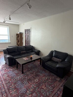 A living room with a sectional sofa, a single chair, a coffee table, and a patterned rug. - Steps from IU Campus & Jacobs School - 1BR Apartment (Bloomington)