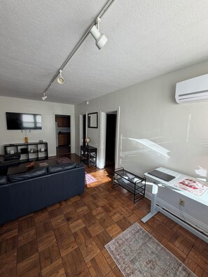 A modern living room with a sofa, TV, and wooden flooring. - Steps from IU Campus & Jacobs School - 1BR Apartment (Bloomington)