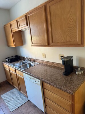 A kitchen with wooden cabinets, a stainless steel sink, a dishwasher, and a coffee maker. - Steps from IU Campus & Jacobs School - 1BR Apartment (Bloomington)