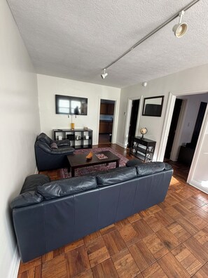 A living room with a dark blue sectional sofa, a coffee table, and a flat-screen TV mounted on the wall. - Steps from IU Campus & Jacobs School - 1BR Apartment (Bloomington)