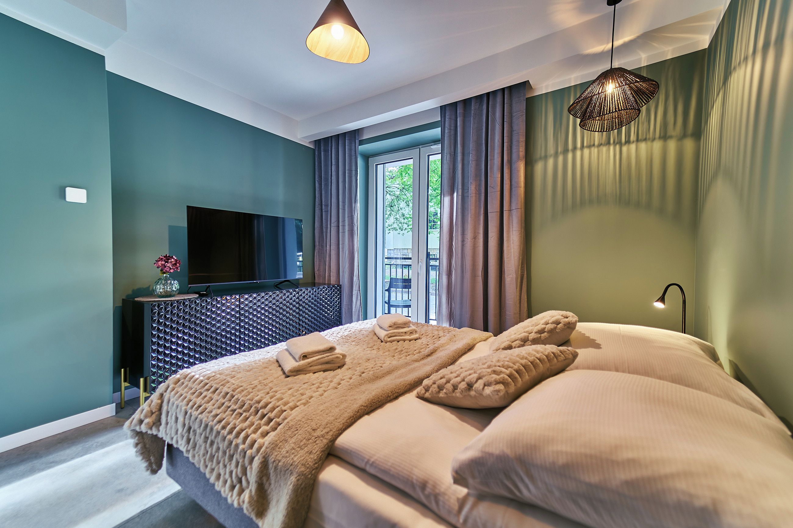 A bedroom with a bed, a TV on a cabinet, and a window with curtains.