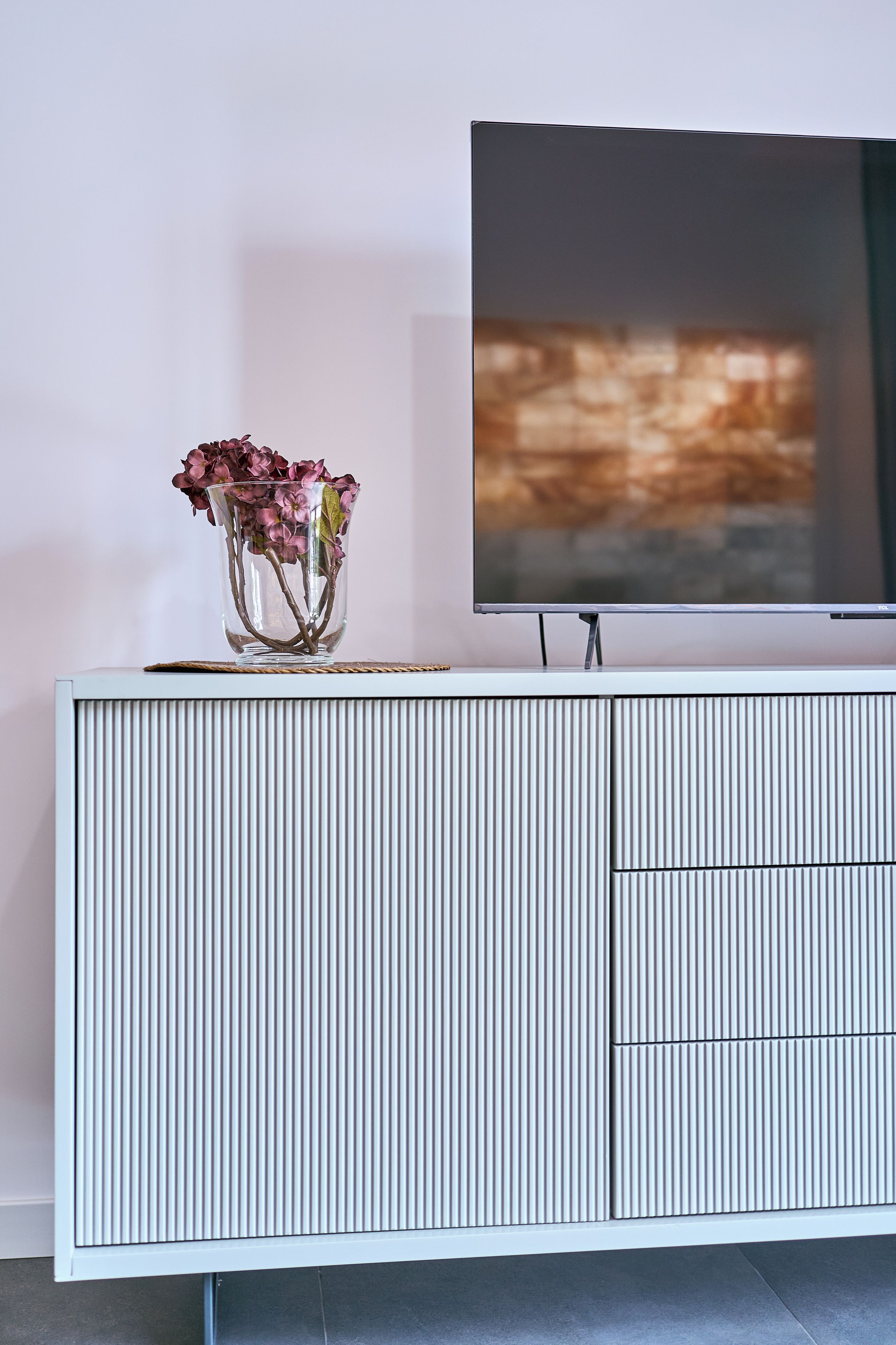 A white, ribbed entertainment center with a flat-screen TV mounted above it.