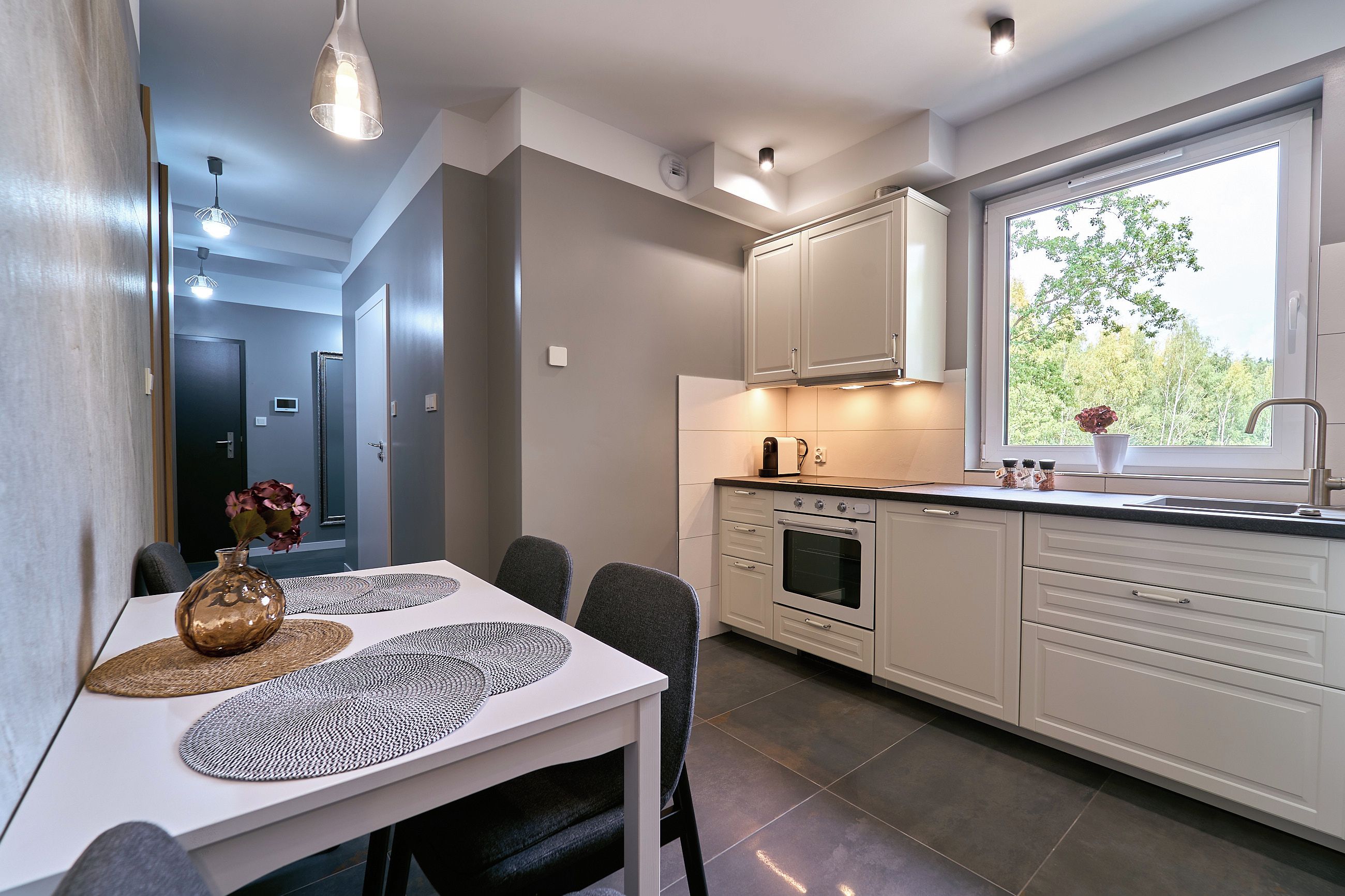 A modern kitchen with white cabinets, a built-in oven, and a window with a view of trees.
