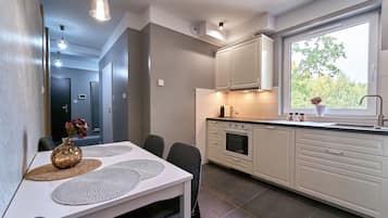A modern kitchen with white cabinets, a built-in oven, and a window with a view of trees.