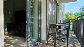 A modern outdoor deck with a dining table and chairs, a sliding glass door leading to a living area, and a wooden fence.