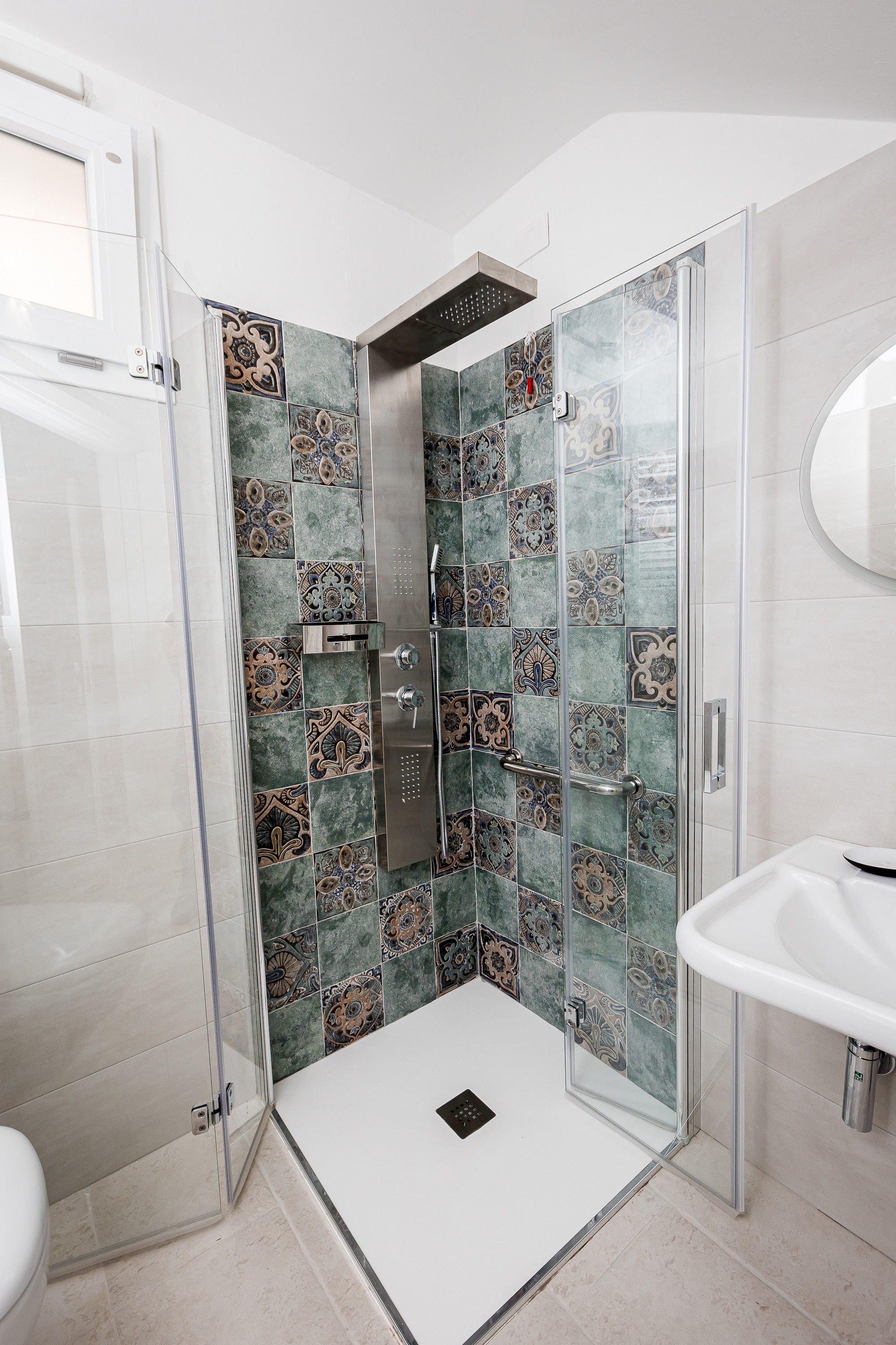 Un baño moderno con cabina de ducha de vidrio, un lavabo blanco y azulejos decorativos.