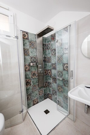 Un baño moderno con cabina de ducha de vidrio, un lavabo blanco y azulejos decorativos.
