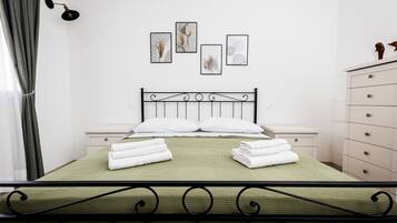 A neatly made bed with white pillows and folded towels, a bedside table, a dresser, and wall-mounted artwork.