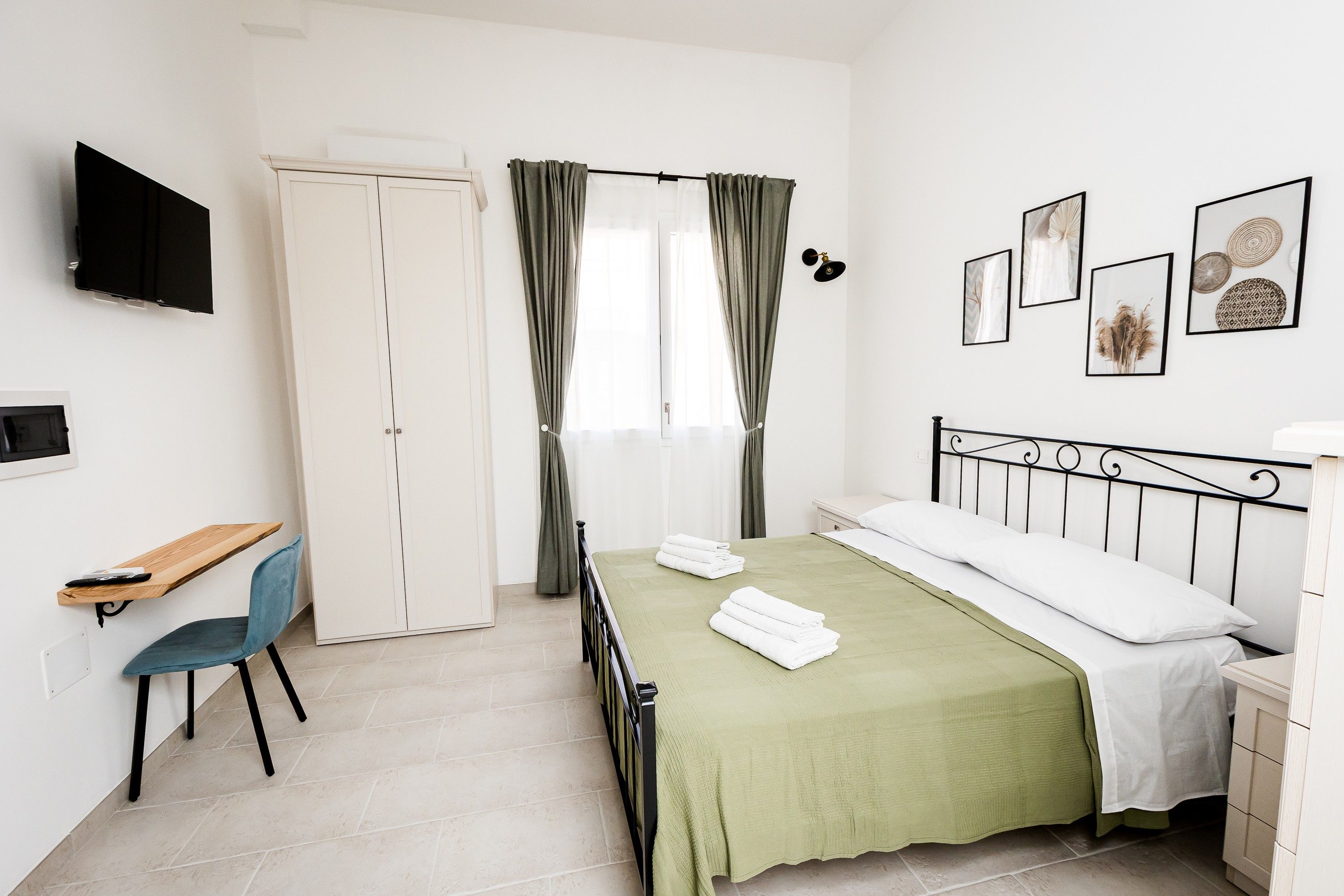 A bedroom with a bed, a desk, a chair, a TV, and a window with curtains.