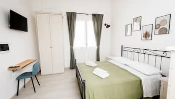 A bedroom with a bed, a desk, a chair, a TV, and a window with curtains.