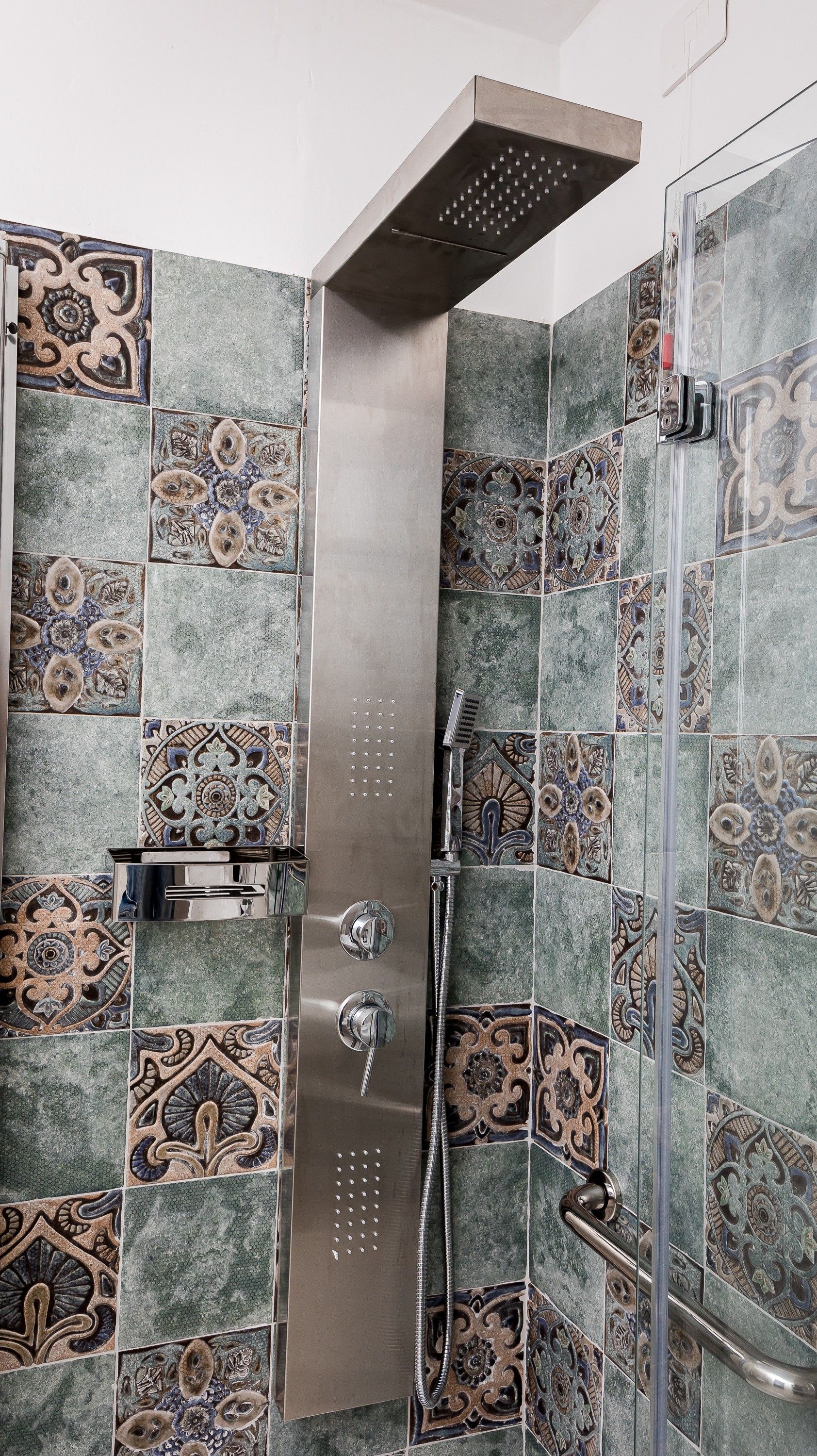A shower with a handheld showerhead and a rain shower head, surrounded by decorative tiles.