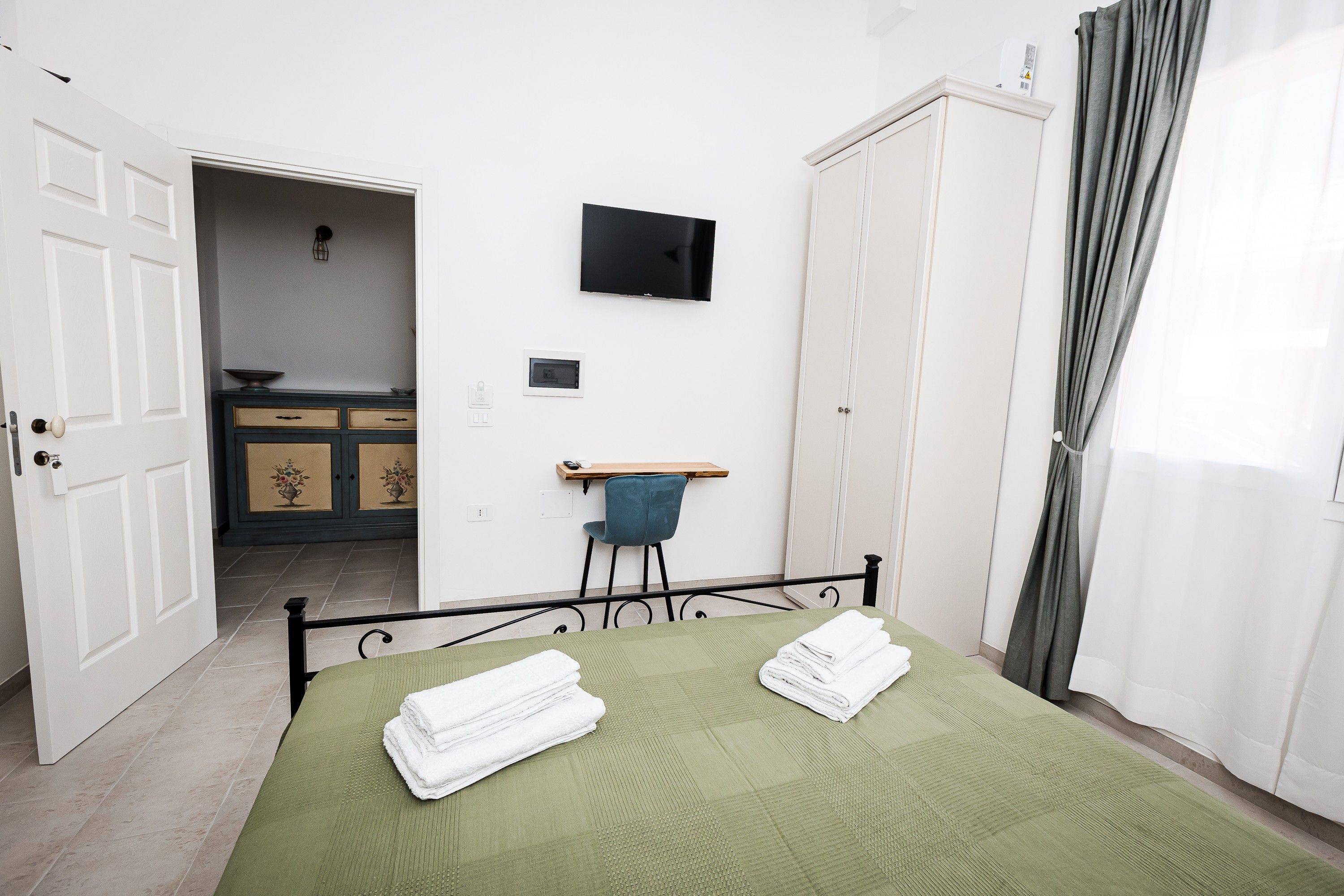 A room with a bed, a television, a wardrobe, and a bathroom visible through an open door.