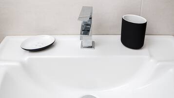 Un lavamanos blanco con grifo cromado y una taza negra a la derecha.