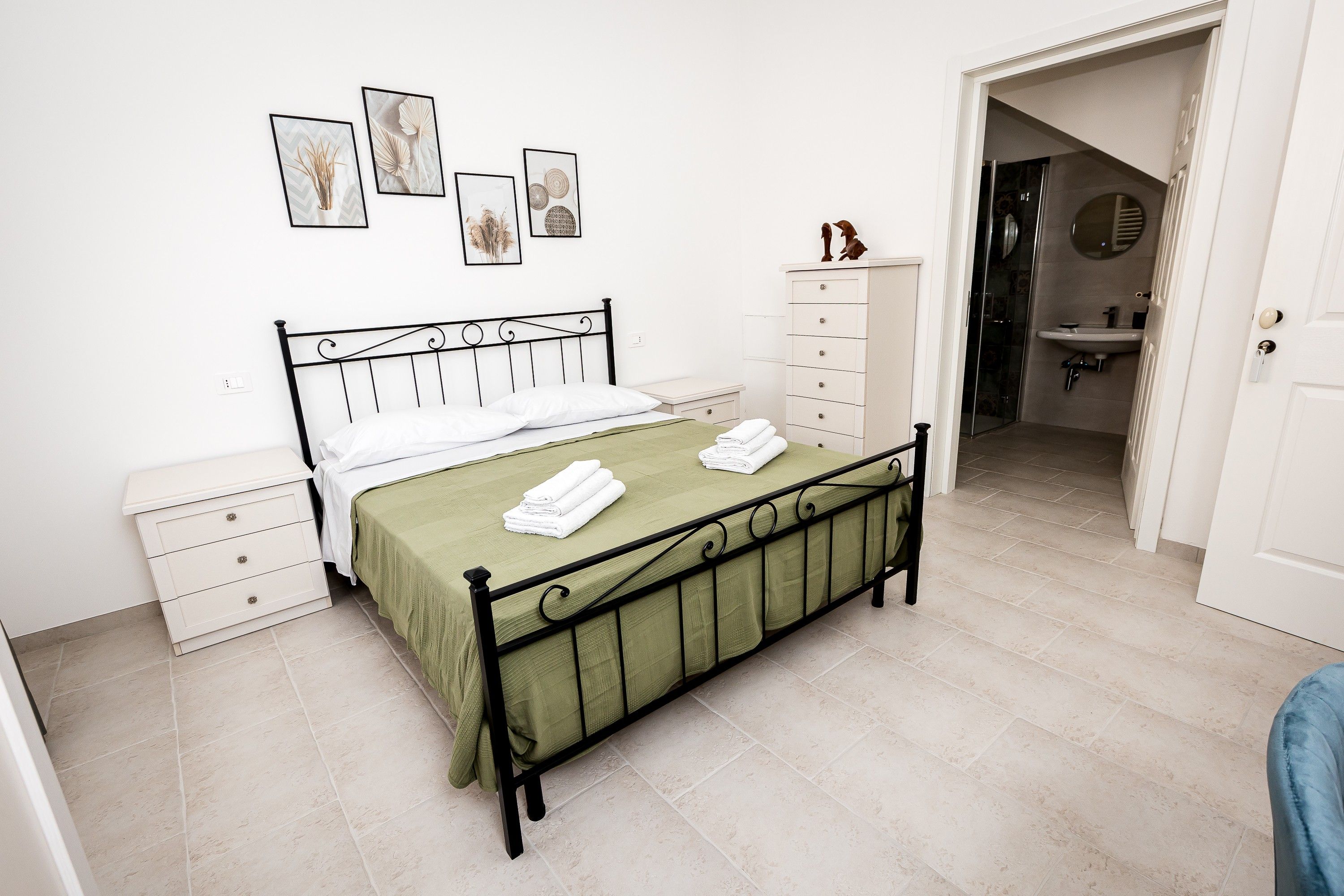 Un dormitorio ordenado con cama, mesitas de noche, cómoda y baño visible a través de una puerta abierta.