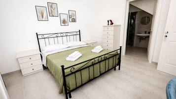 Un dormitorio ordenado con cama, mesitas de noche, cómoda y baño visible a través de una puerta abierta.