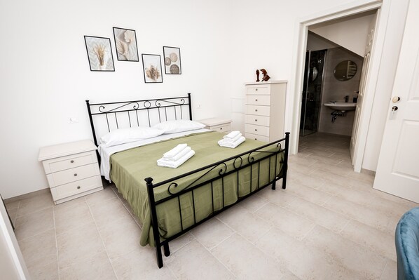 Un dormitorio ordenado con cama, mesitas de noche, cómoda y baño visible a través de una puerta abierta.