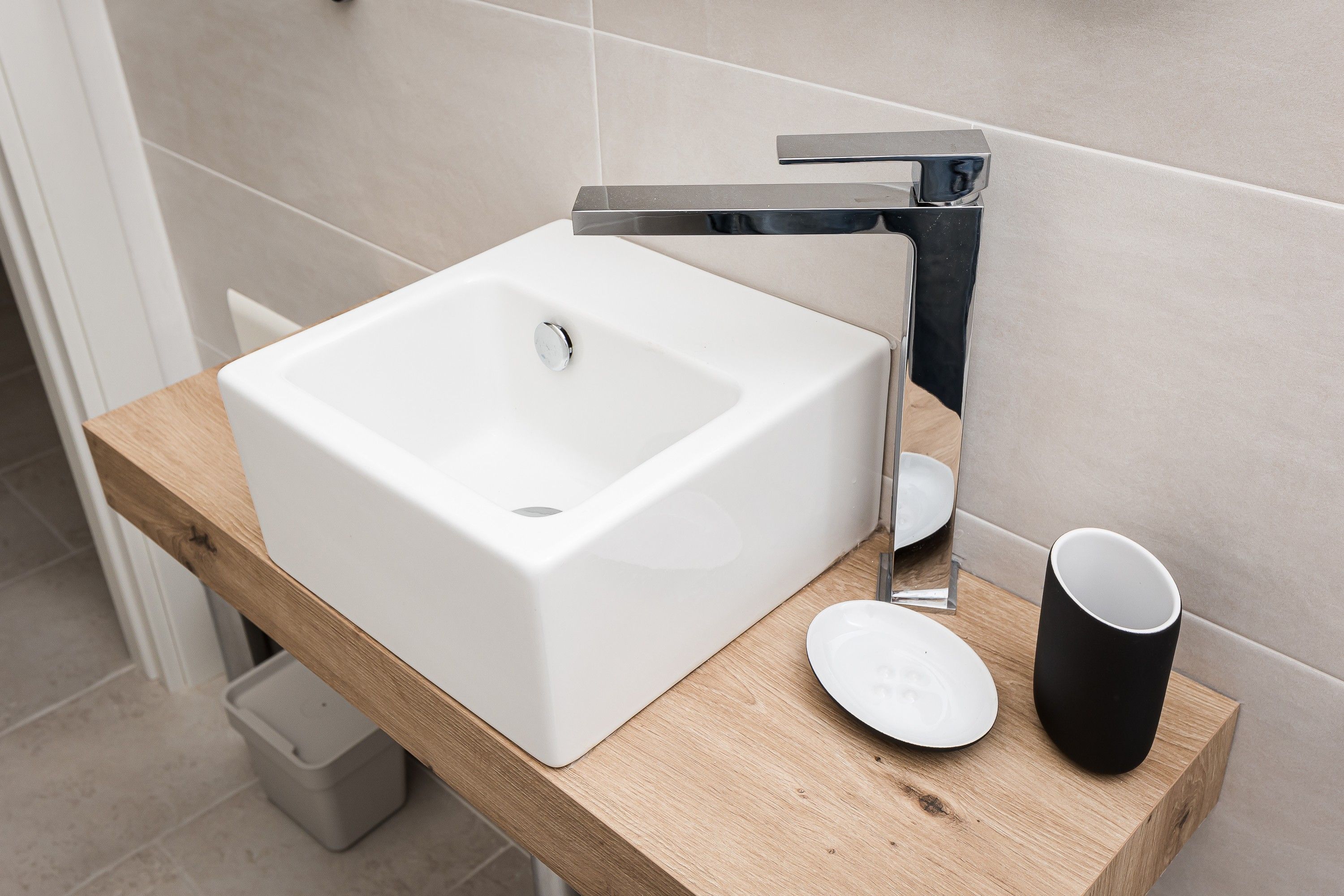 Un baño moderno con un lavabo blanco, grifo cromado y encimera de madera.