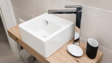 Un baño moderno con un lavabo blanco, grifo cromado y encimera de madera.