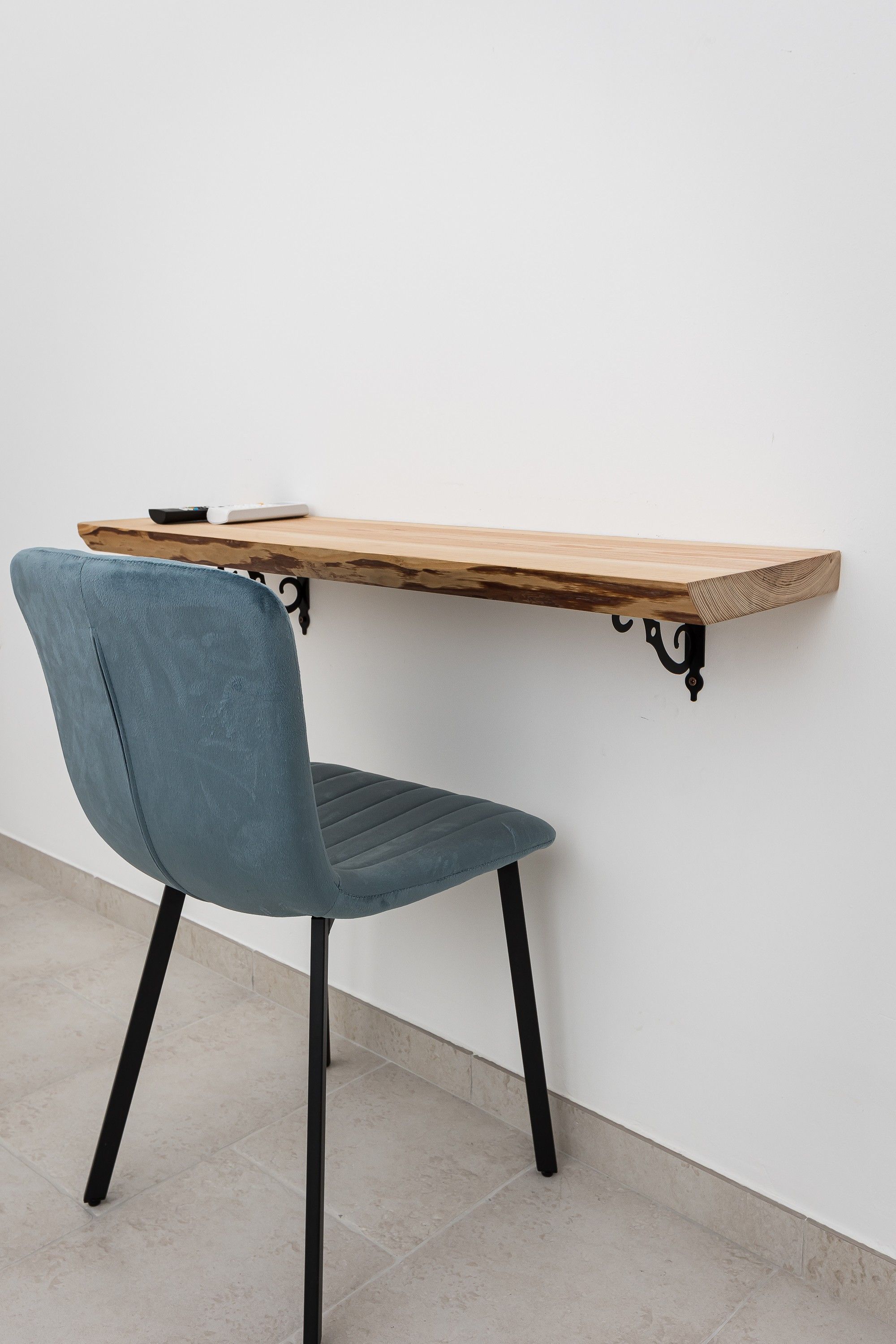 A chair with a backrest and seat, a wooden table with a black metal frame, and a white wall.