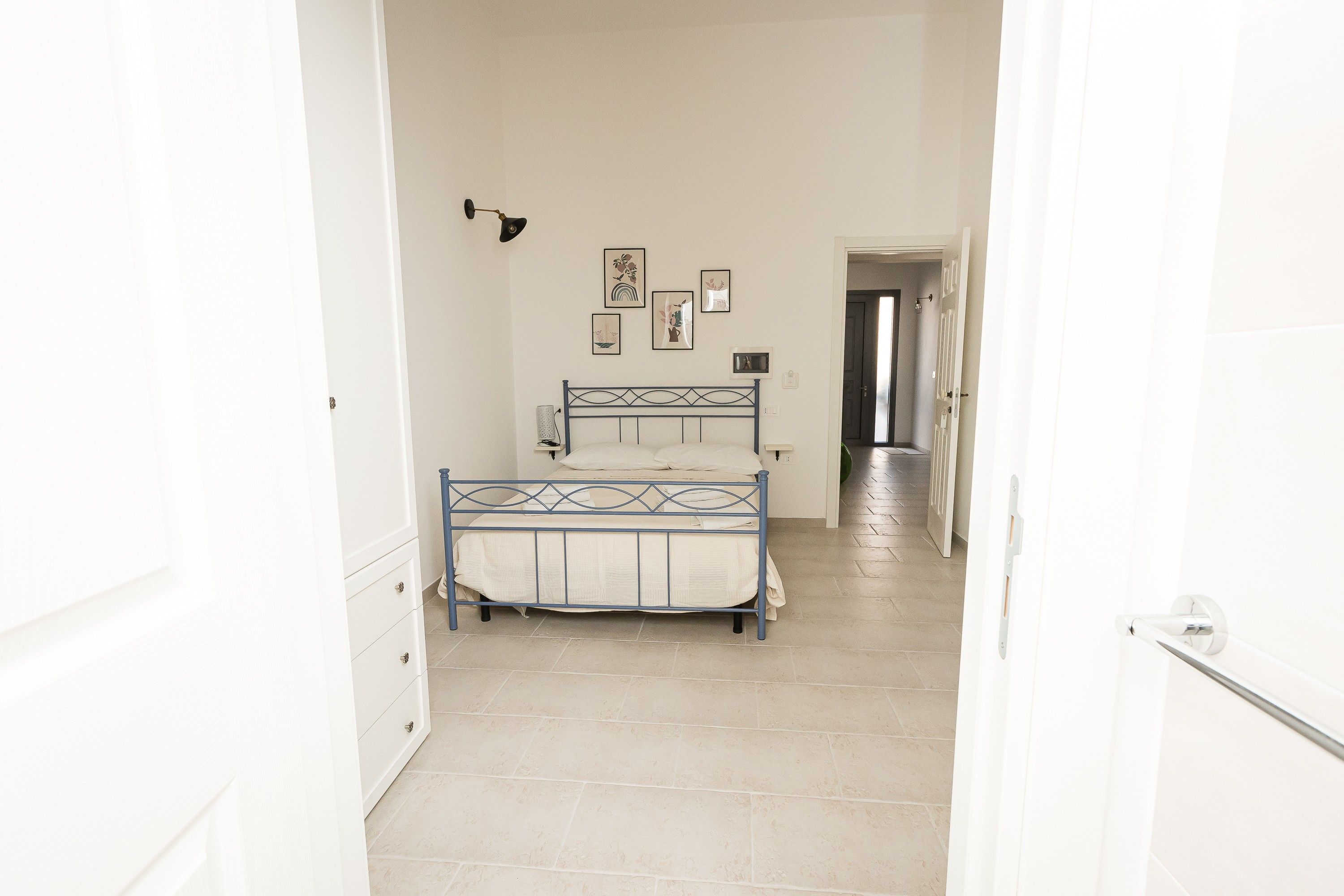 A bedroom with a bed, a dresser, and a hallway leading to another room.
