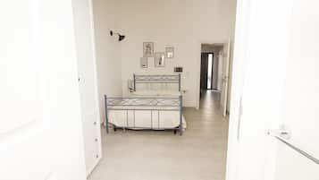 A bedroom with a bed, a dresser, and a hallway leading to another room.