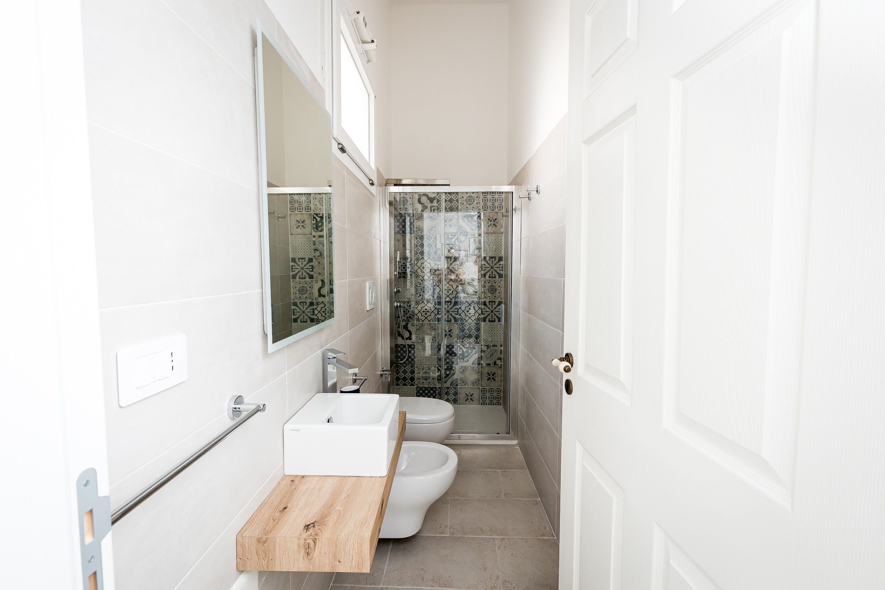 A narrow bathroom with a white sink, a toilet, and a shower area.
