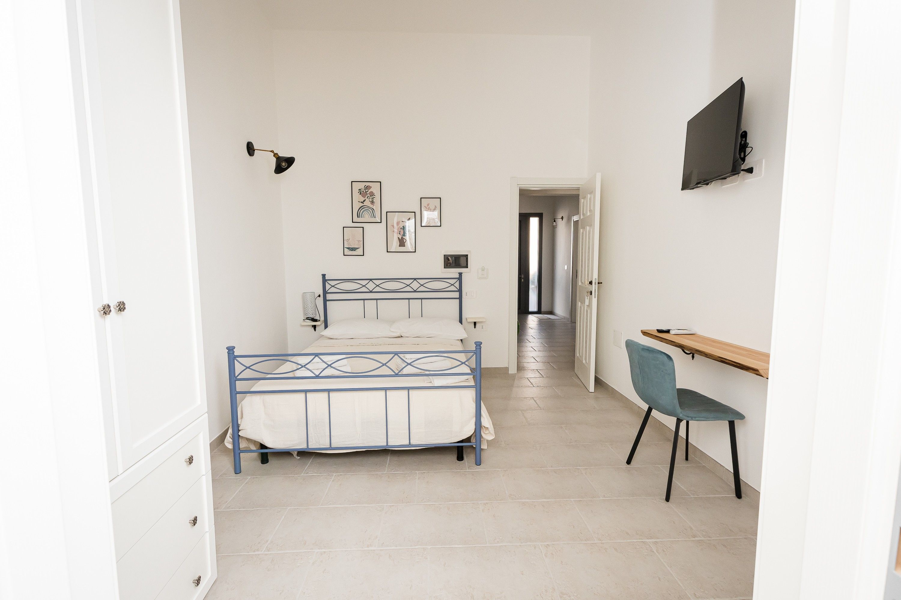 Un dormitorio con cama, escritorio, silla y televisor en la pared.