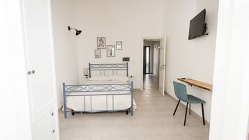 Un dormitorio con cama, escritorio, silla y televisor en la pared.