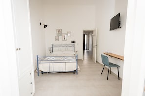 Un dormitorio con cama, escritorio, silla y televisor en la pared.