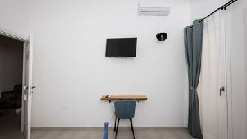 Una habitación con una televisión de pantalla plana montada en la pared, un estante de madera, una silla y una cortina.