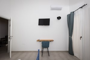 Una habitación con una televisión de pantalla plana montada en la pared, un estante de madera, una silla y una cortina.