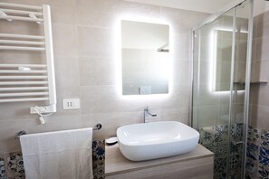 Een badkamer met een wit wastafelmeubel, een douchecabine van glas en een handdoekrek.