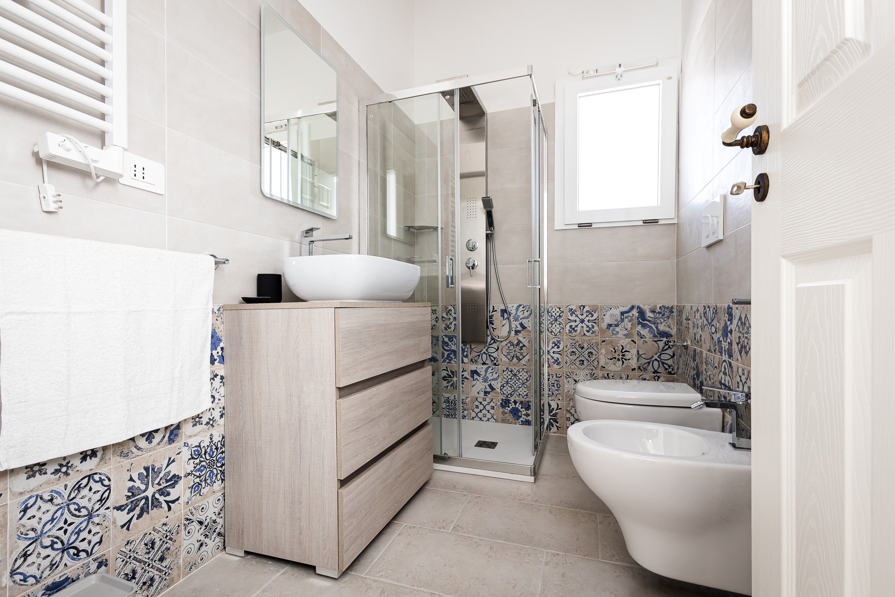 A bathroom with a white sink, a wooden vanity, a glass shower enclosure, and a toilet.