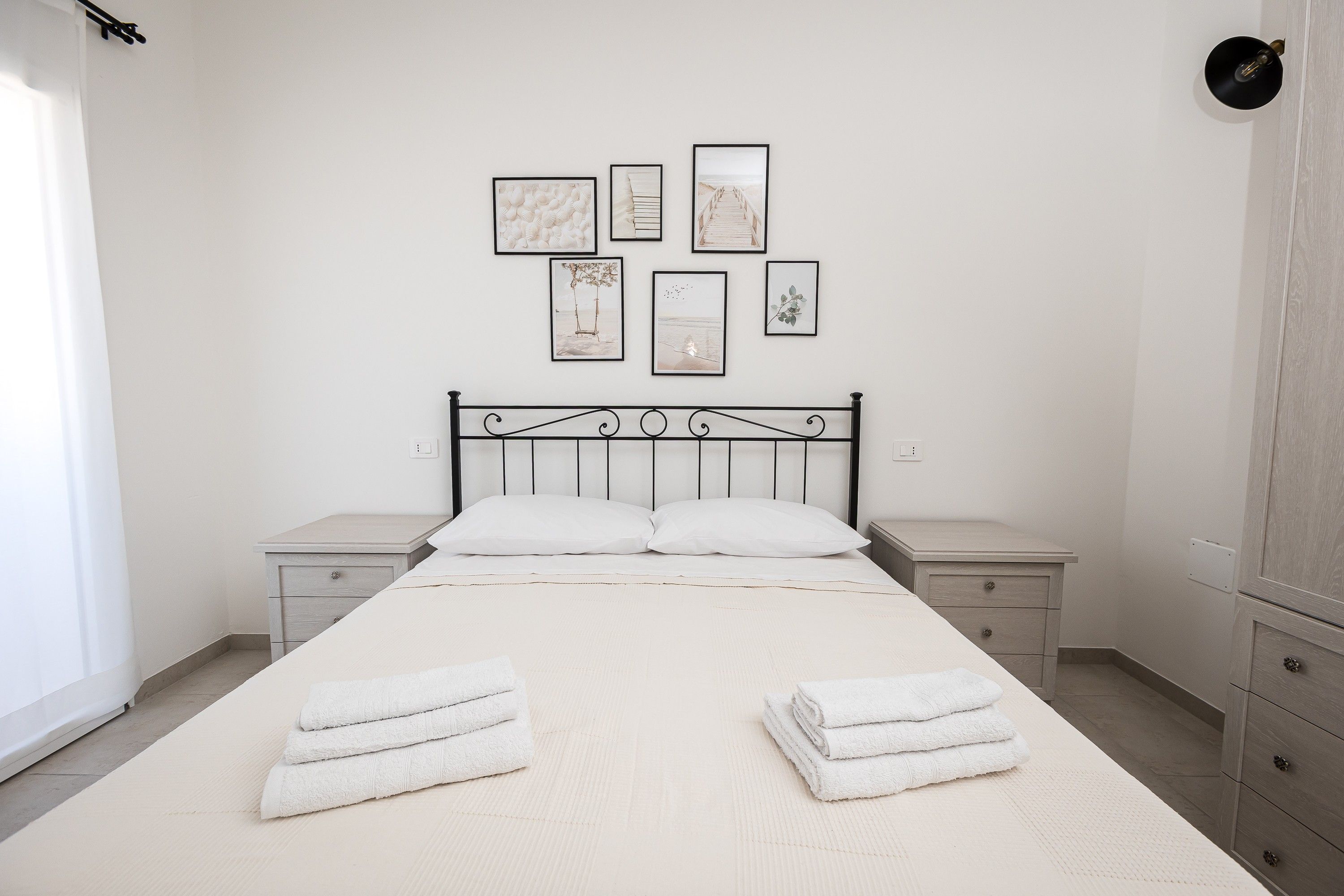 A bedroom with a bed, two nightstands, a wall with framed pictures, and a wardrobe.