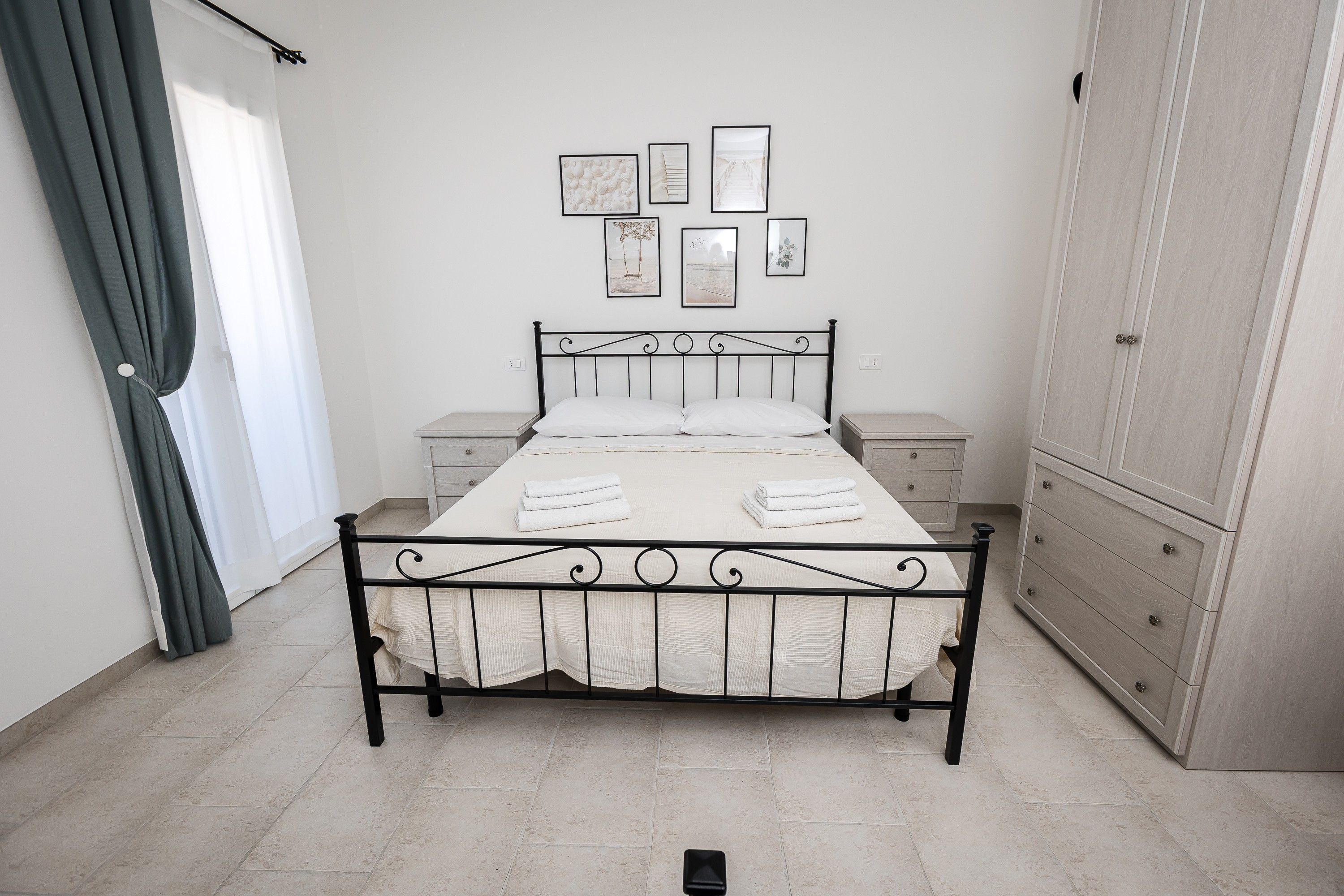 Un dormitorio con cama, mesitas de noche, un armario y una pared adornada con cuadros.