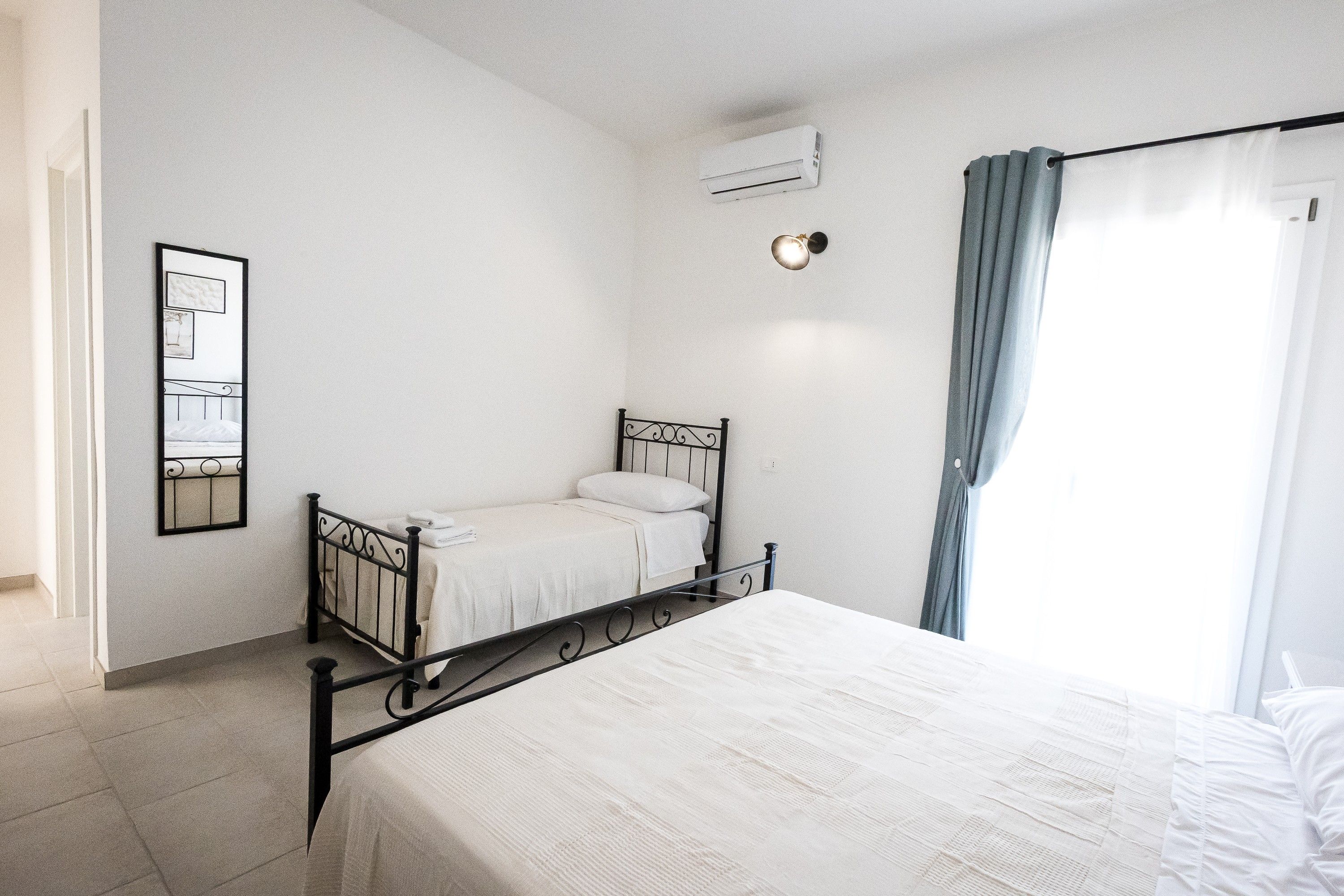 Un dormitorio con una cama individual, una mesita de noche, aire acondicionado instalado en la pared y una ventana con cortinas.