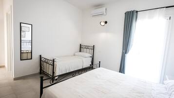 Un dormitorio con una cama individual, una mesita de noche, aire acondicionado instalado en la pared y una ventana con cortinas.