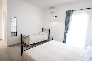 Un dormitorio con una cama individual, una mesita de noche, aire acondicionado instalado en la pared y una ventana con cortinas.